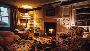 Un salon chaleureux avec une cheminée, des fauteuils à motifs floraux, une bibliothèque et une lampe.