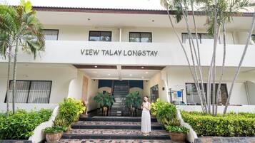 Entrada de hotel com uma placa indicando 'VIEW TALAY LONGSTAY', uma escadaria e plantas em vasos.