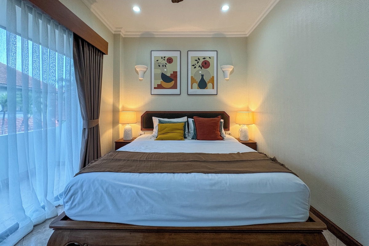 Una habitación de hotel con una cama, dos lámparas fijadas a la pared y dos cuadros enmarcados sobre la cama.