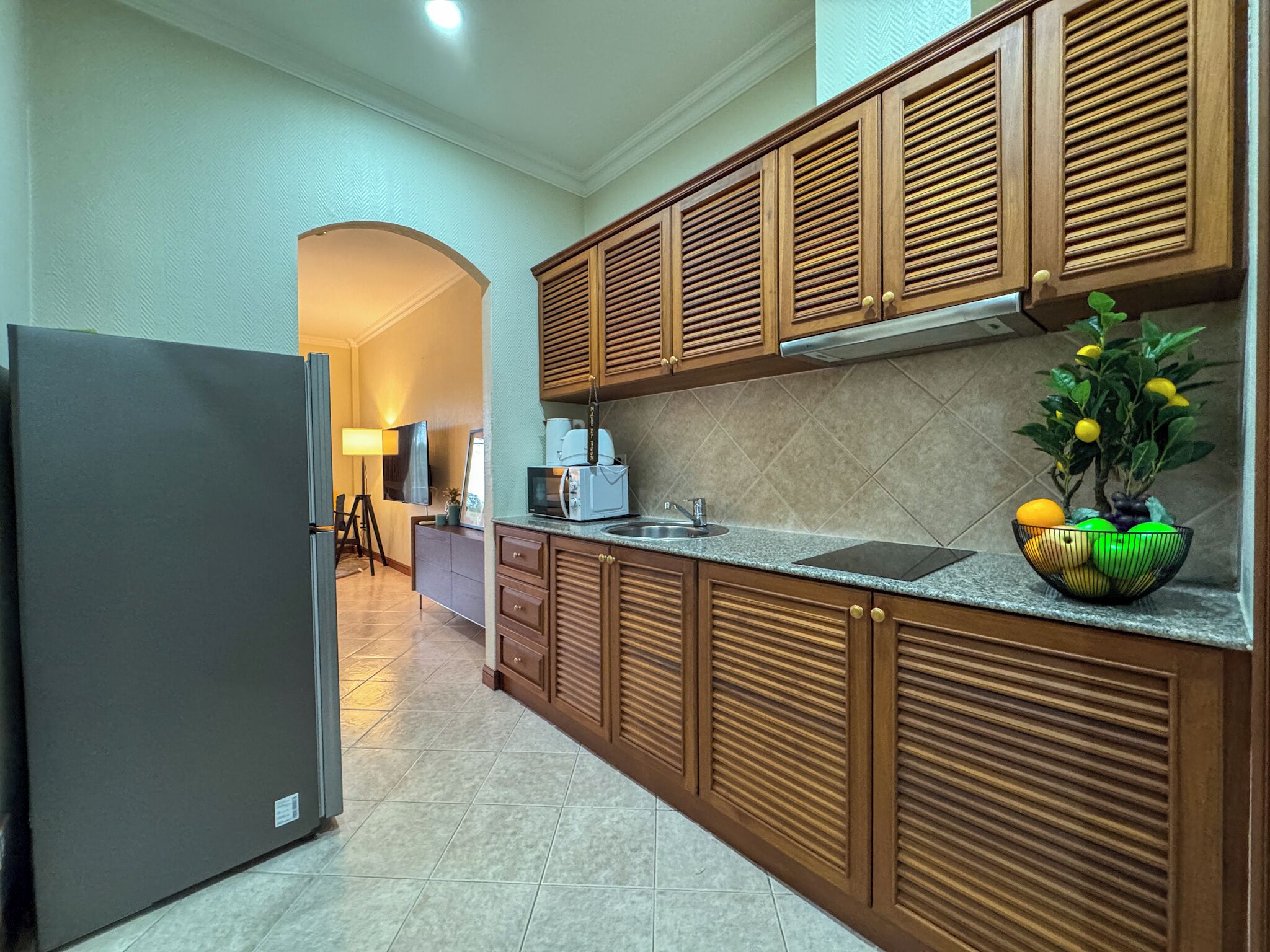 A modern kitchen with wooden cabinets, a refrigerator, a sink, and a countertop with a fruit bowl.