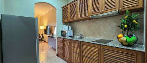 A modern kitchen with wooden cabinets, a refrigerator, a sink, and a countertop with a fruit bowl.