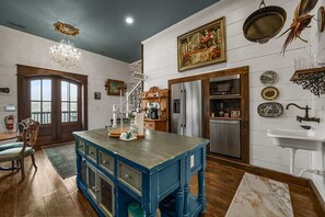 A kitchen with a central island, a refrigerator, and a sink. There is a chandelier, a painting, and various kitchen utensils on the walls. - High End Design Near Downtown Gatlinburg/Views (Gatlinburg)