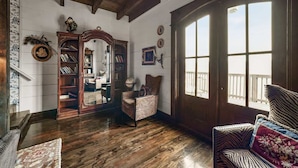 Ein geräumiges Zimmer mit Holzböden, einem großen Fenster mit Blick und einem Bücherregal sowie einem Sessel.