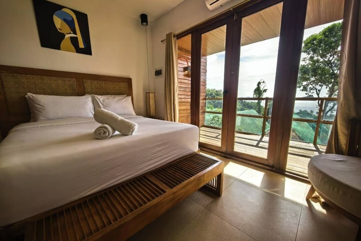 Ein Schlafzimmer mit Bett, einer Bank, einem Fenster und Blick ins Grüne.