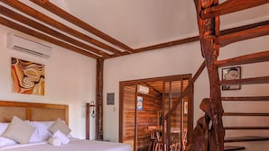 A wooden-framed bedroom with a bed, a wooden sculpture, and a dining area visible through a glass door.