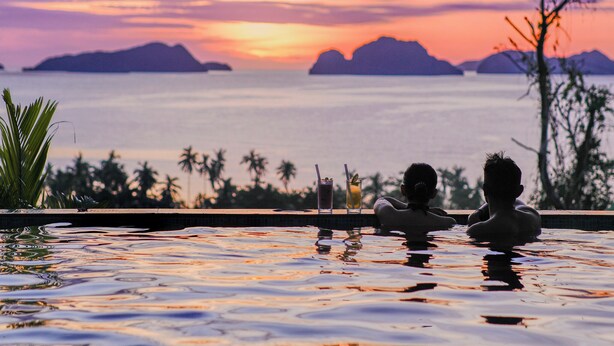 A pool with two people in the water, a sunset, and distant mountains.