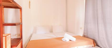 A single bed with a white mattress and orange bedding, a wooden shelf unit, and a grey curtain.