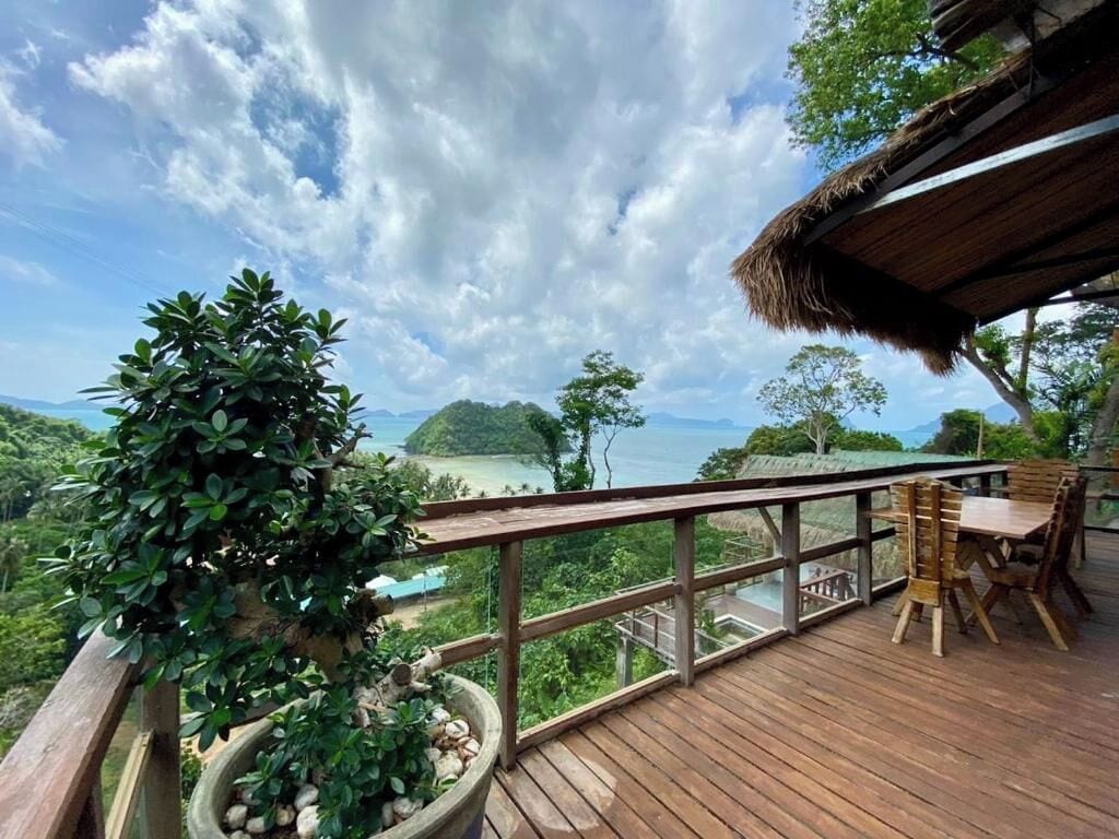 A wooden deck with a table and chairs, overlooking a scenic landscape with mountains and a body of water.