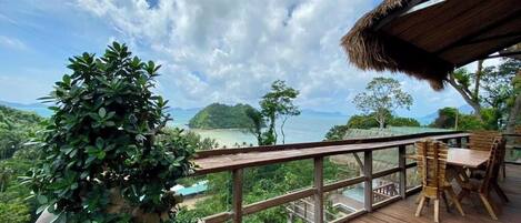 A wooden deck with a table and chairs, overlooking a scenic landscape with mountains and a body of water.