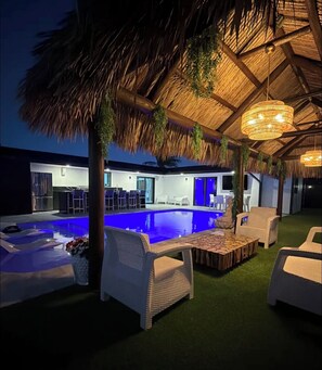 A modern outdoor pool area with a thatched roof, lounge chairs, and a bar area. - Hollywood - Private Pool • Tiki Hut. Modern Home - Sleeps 6 (Pembroke Pines)