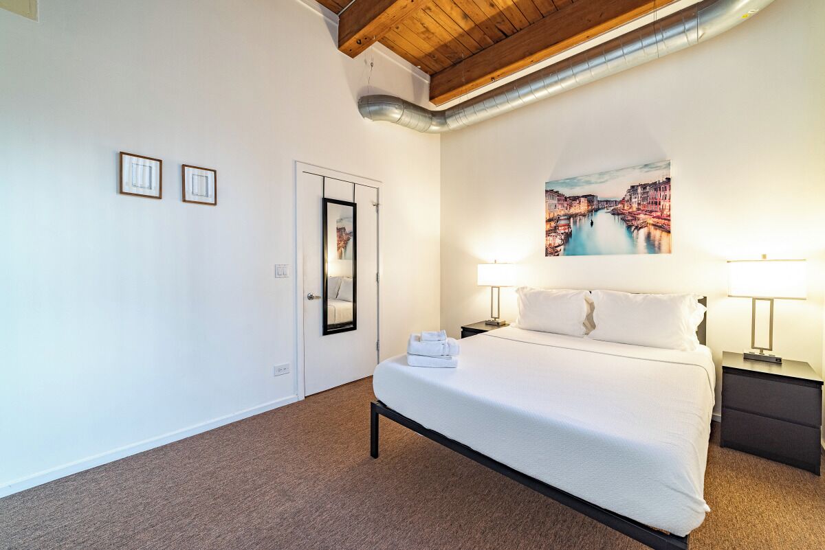 Een hotelkamer met een bed, twee bedlampen, een schilderij aan de muur en een deur.