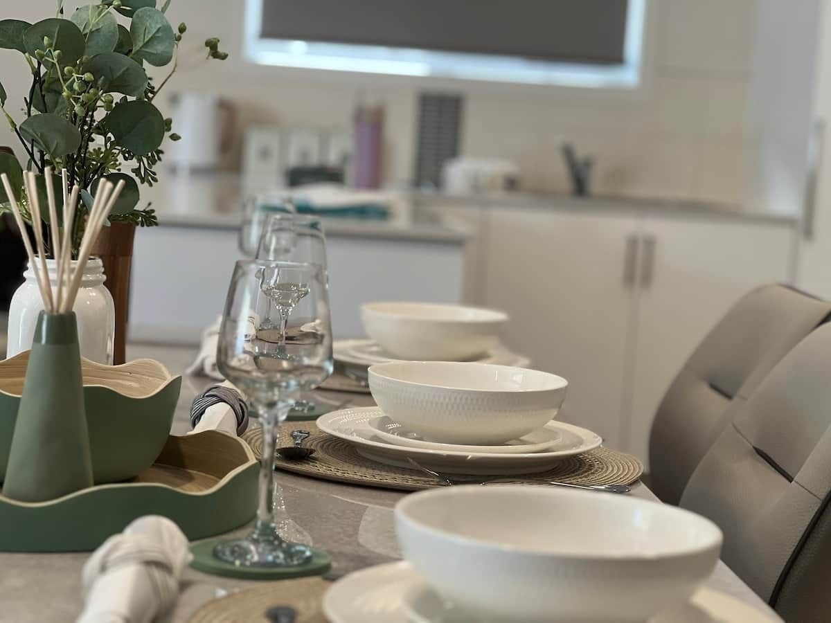A dining table set with white bowls, plates, and a glass of water.