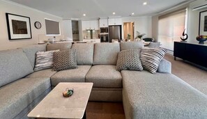 A modern living room with a sectional sofa, a coffee table, and a kitchen in the background. - Cambridge Opening Special prices, enjoy the newness (Mornington)