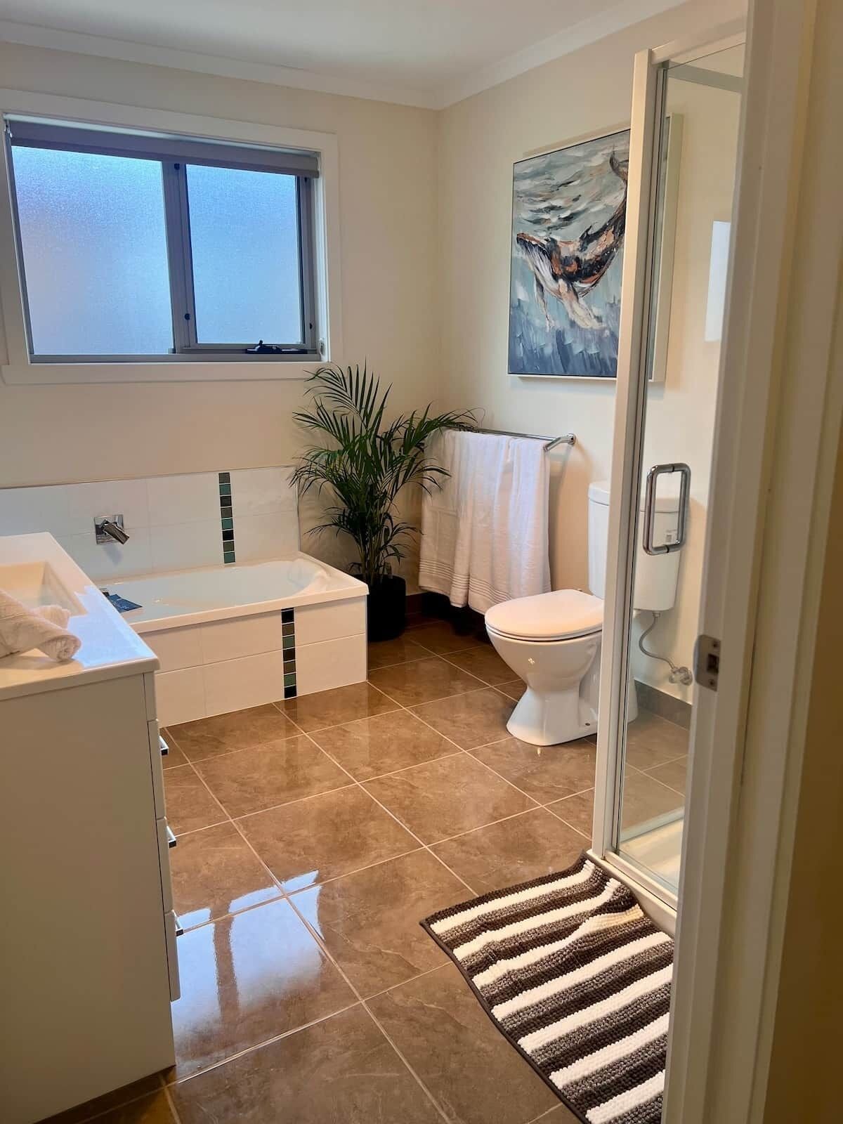 Een moderne badkamer met een bad, toilet en een groot raam.
