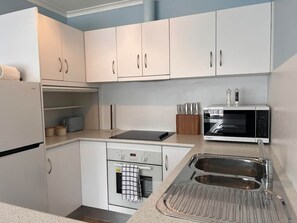 A compact kitchen with white cabinets, a microwave, a stove, and a sink. - Howrah Apartment (Howrah)