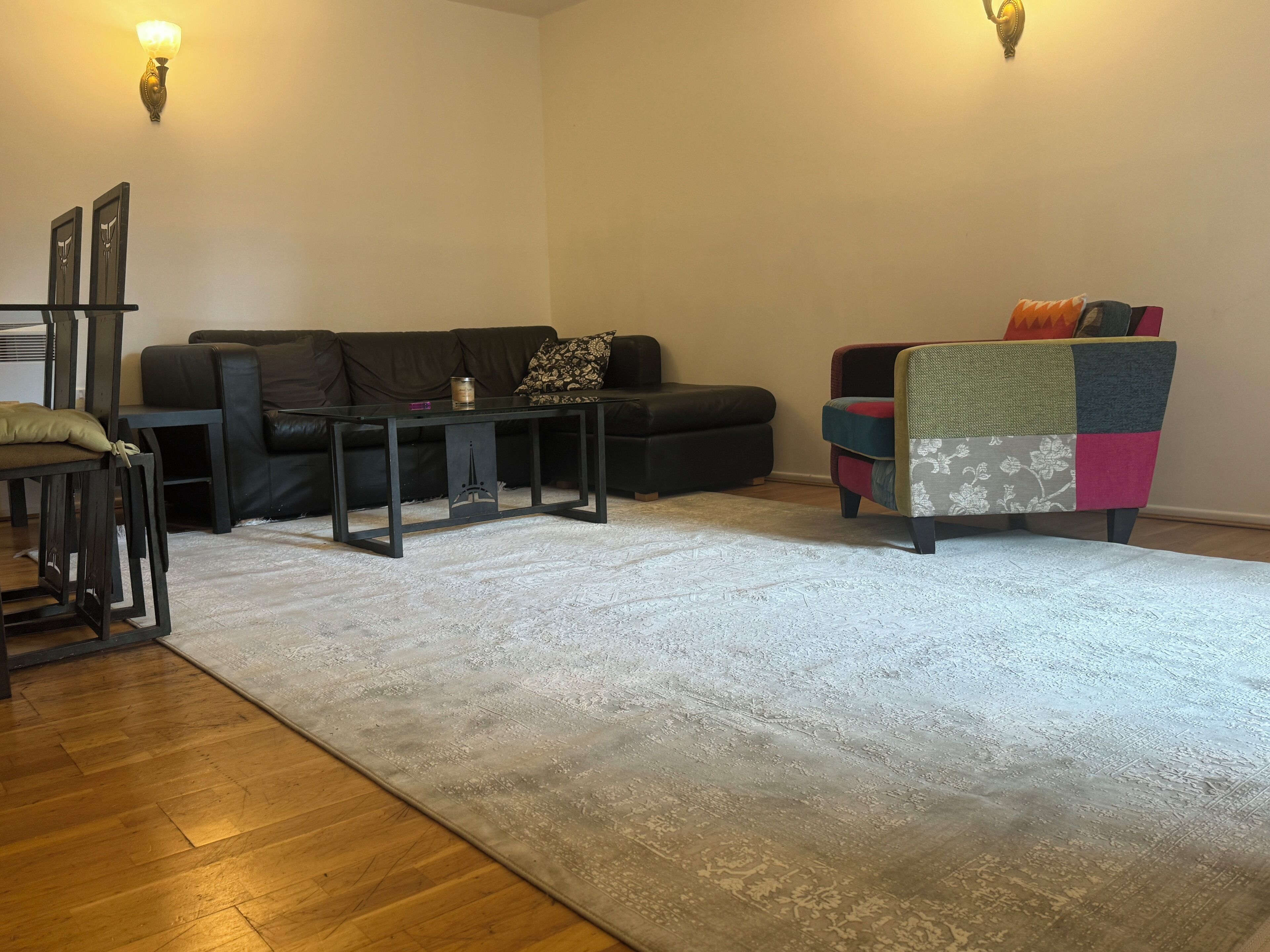 A living room with a black leather sofa, a glass coffee table, a colorful armchair, and a patterned rug.