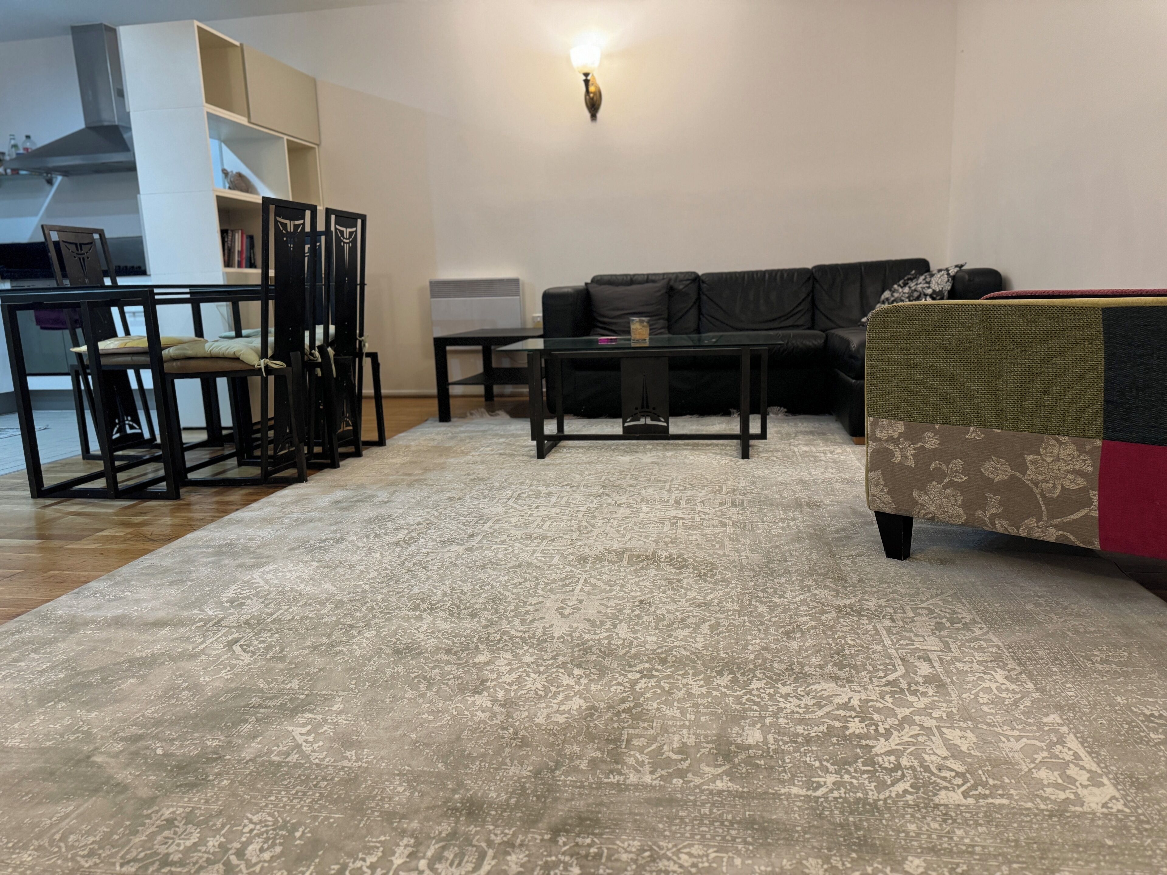 A modern living room with a black sofa, a patterned rug, and a dining area with a black table and chairs.
