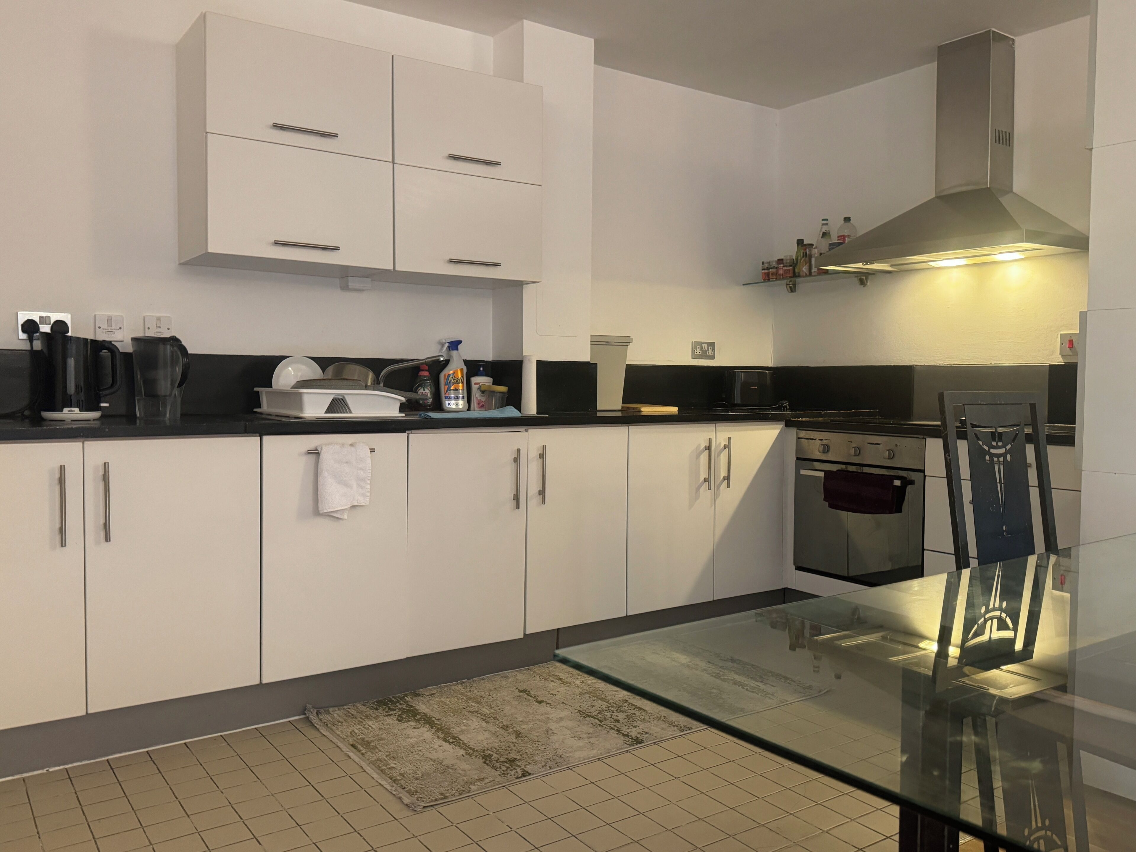 A modern kitchen with white cabinets, a stainless steel range hood, and a glass dining table.