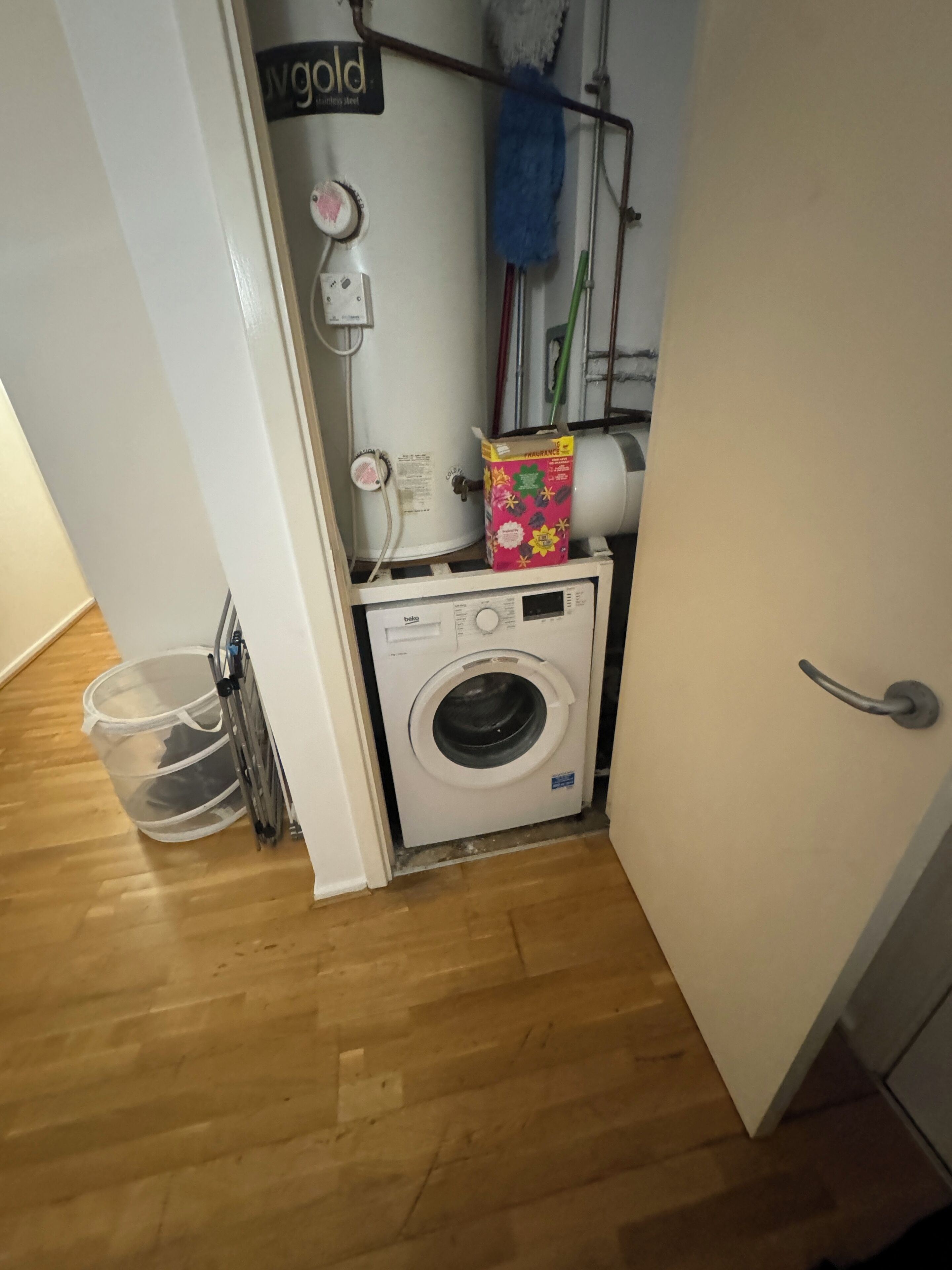 A compact laundry room with a front-loading washing machine, a drying rack, and a storage bin.