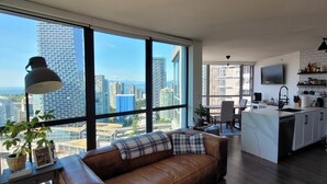 A modern apartment with a large window, a brown leather sofa, a dining area, and a kitchen. - 29th Floor Condo in Yaletown. Message me at a.hostacny@gmail.com for details 
 (Vancouver)