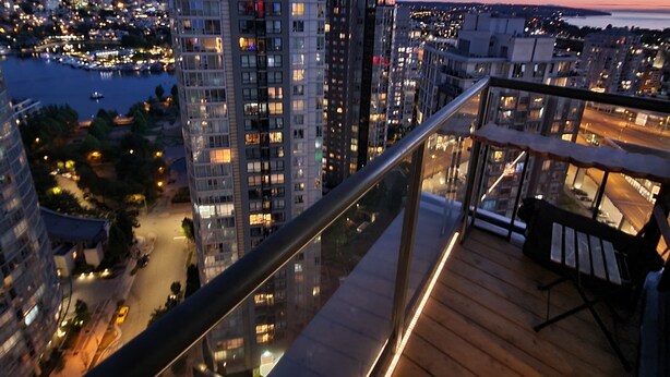 A high-rise building with multiple floors, a balcony with wooden flooring, and a view of a cityscape at dusk. - 29th Floor Condo in Yaletown. Message me at a.hostacny@gmail.com for details 
 (Vancouver)