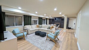 Ein geräumiges Wohnzimmer mit einem Ecksofa, zwei Sessel, einem Couchtisch und einem Kamin.