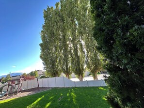 A residential backyard with a white fence, a swing set, and a tall tree. - Cozy 3BR private basement unit by SF River trail in Spanish Fork (Spanish Fork)