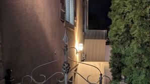 Ein schmiedeeisernes Tor mit Verzierungen, eine Wandleuchte und ein gepflegter Heckenstreifen.