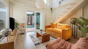 Un salon moderne avec un canapé, une table basse et un téléviseur. On y trouve un escalier, et une plante est placée sur la plateforme entre les étages.