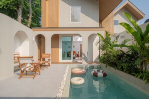 Une maison moderne dotée d’une piscine, de chaises longues en bois et d’une entrée avec une porte en verre.
