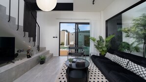 Un salon moderne avec un canapé noir, une table basse ronde, un téléviseur et un escalier doté de rampes noires.
