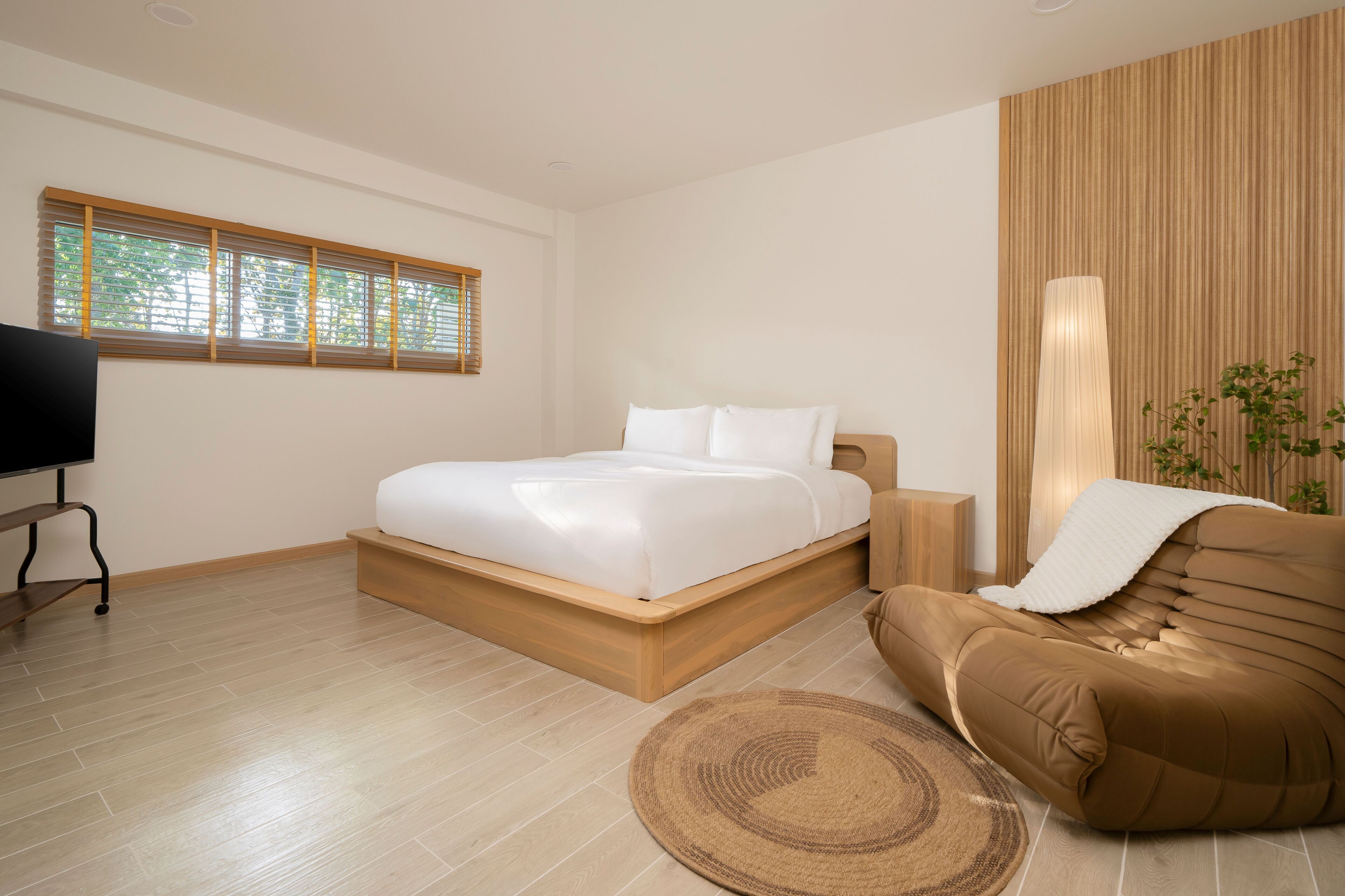 A modern bedroom with a wooden bed frame, a flat-screen TV, and a brown armchair.
