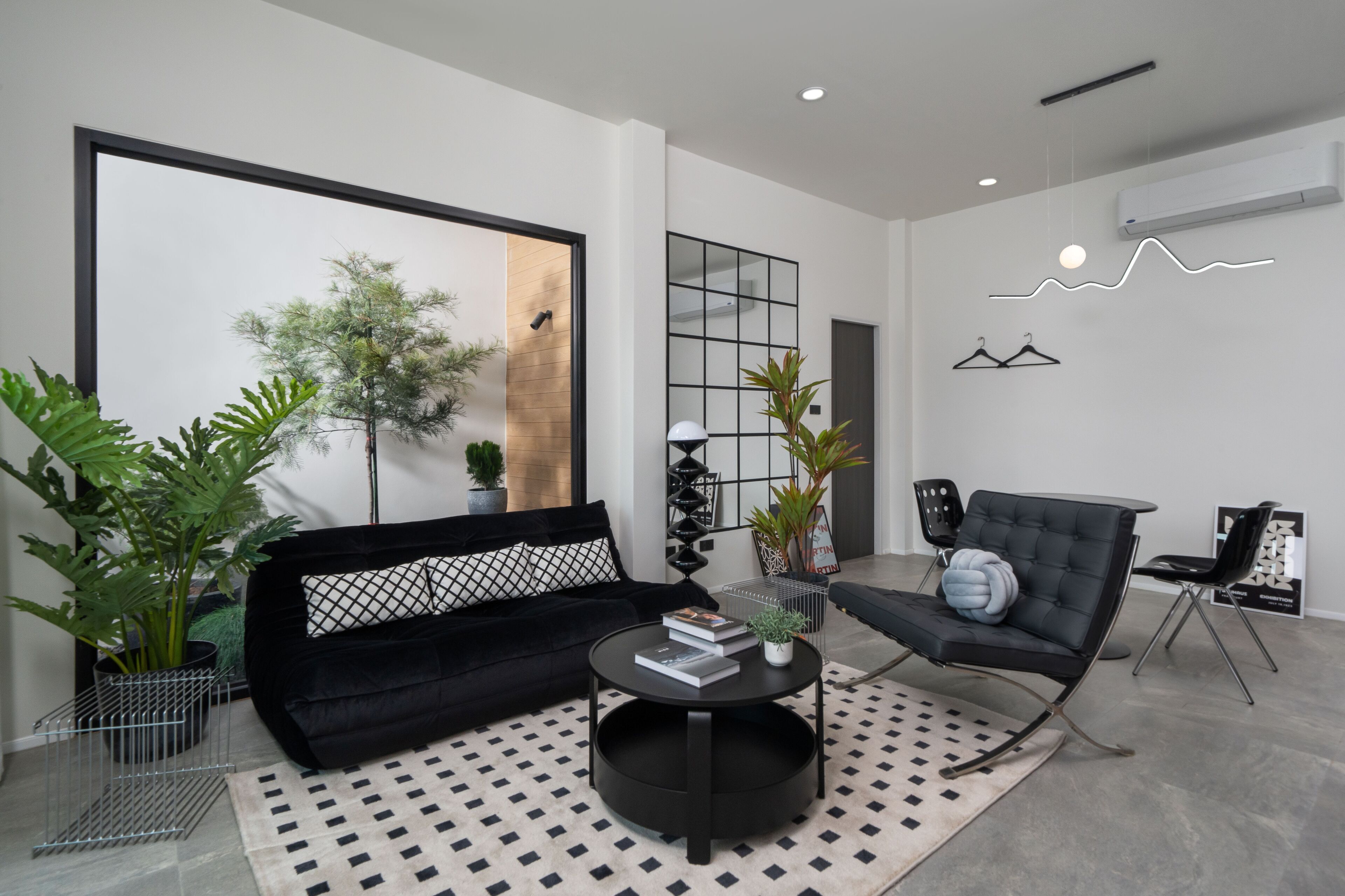 Una sala de estar moderna con un sofá negro, una mesita redonda y un sillón negro. Hay plantas en macetas y un espejo grande en la pared.