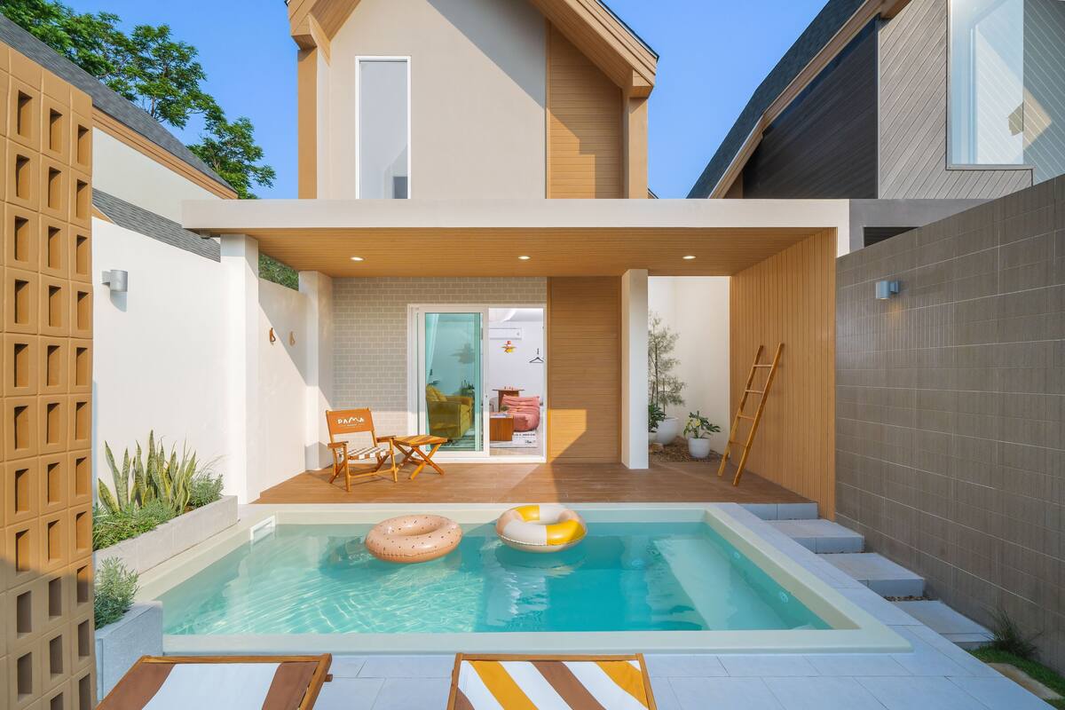 Una casa moderna con piscina, mobiliario exterior y una terraza de madera.