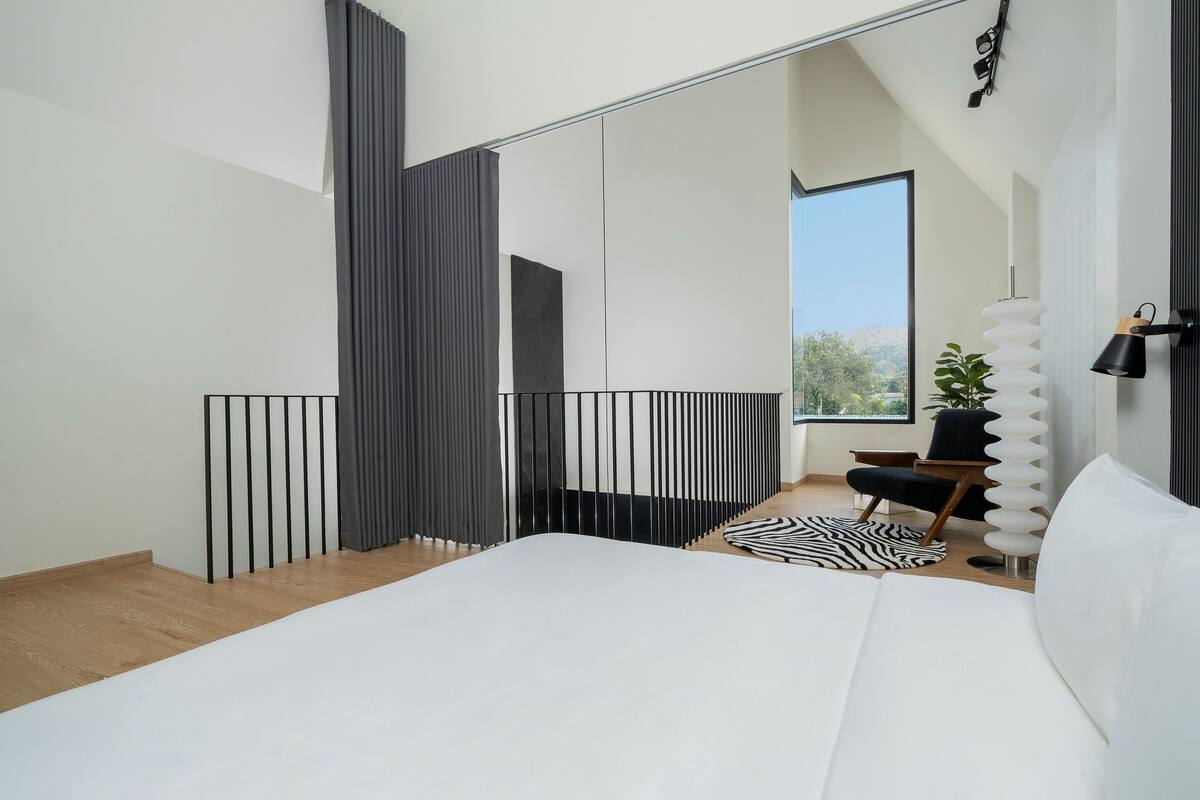 Un dormitorio moderno con una cama grande, vistas al exterior, un tapete con estampado blanco y negro, y una silla negra.