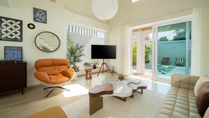 Un salon moderne doté d’un grand téléviseur, de sièges confortables et offrant une vue sur une piscine.