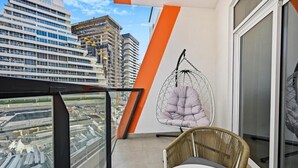 En balkon med hængestol, fletstol og et bord.