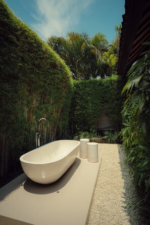 Une salle de bain moderne avec une baignoire sur pieds, des toilettes et un lavabo, le tout entouré d’une végétation luxuriante.