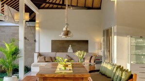 A modern living room with a wooden ceiling, a sofa set, a dining table, and a bench. - Sahana Villas (Seminyak)
