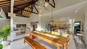 A spacious living area with a wooden dining table, a sofa, and a large window. - Sahana Villas (Seminyak)