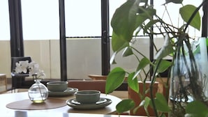 Une table à manger ornée d’un vase de fleurs blanches, de deux bols et d’un vase en verre contenant des feuilles vertes.