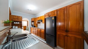 A kitchen with wooden cabinets, a black refrigerator, a microwave, and a sink. - Room for Everyone Spacious 4BR Pool Retreat (Kirwan)