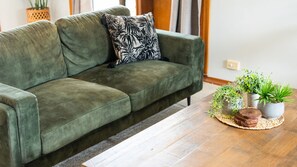 A green sofa with a patterned pillow, a wooden coffee table with potted plants, and a woven rug. - Room for Everyone Spacious 4BR Pool Retreat (Kirwan)