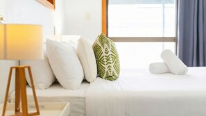 Una camera d'albergo con un letto, cuscini, una lampada e una finestra con tende.