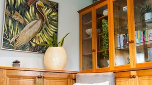 A room with a wooden cabinet containing books, a large painting of a bird, and a textured vase with green leaves. - Room for Everyone Spacious 4BR Pool Retreat (Kirwan)