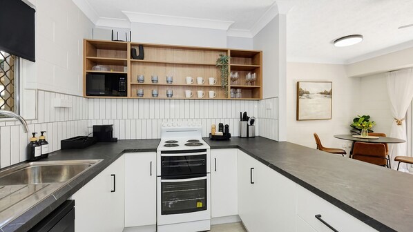A modern kitchen with white cabinetry, a built-in oven, and a microwave. There is a dining area with a table and chairs.