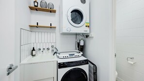 A compact laundry room with a front-loading washing machine, a sink, and a drying rack.
