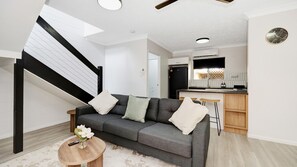 A modern living room with a grey sofa, a small round coffee table, and a staircase with black railings.