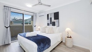 A hotel room with a bed, a ceiling fan, a window with curtains, and a wall-mounted air conditioning unit.
