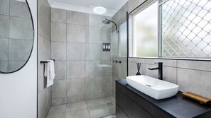 Ein modernes Badezimmer mit einem großen Spiegel, einer Dusche und einem Waschbecken.